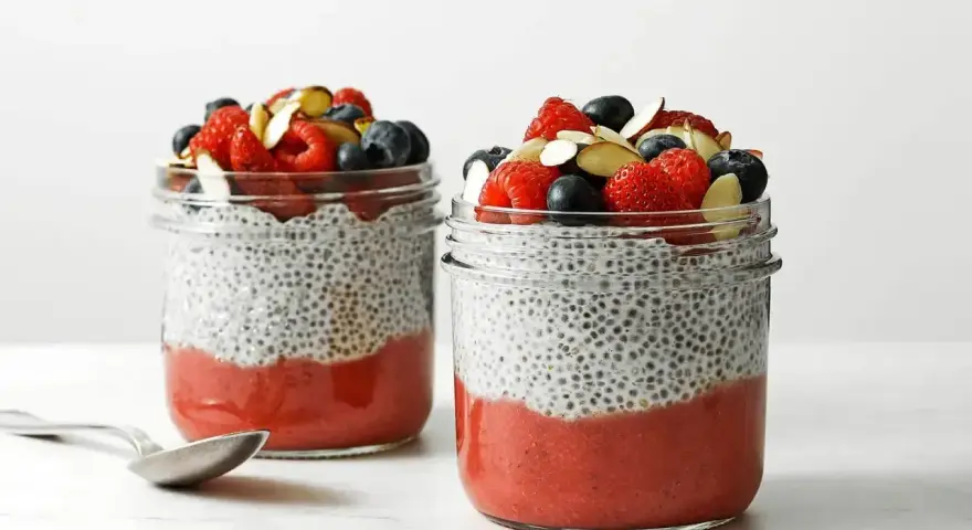 Pyszny pudding chia przepis: warstwy musu truskawkowego i nasion chia, zwieńczone świeżymi owocami i migdałami.
