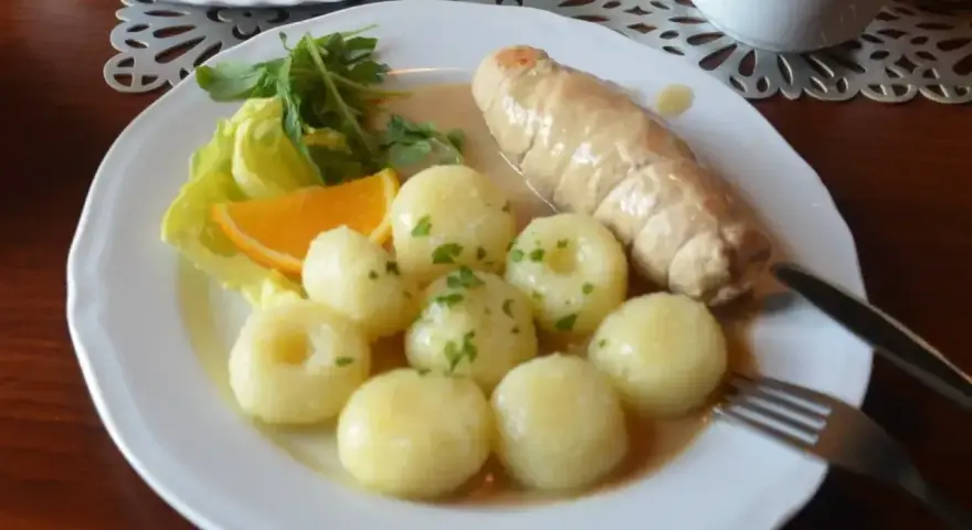 Pyszne kluski śląskie z roladą mięsną, surówką z czerwonej kapusty i plasterkiem pomarańczy.