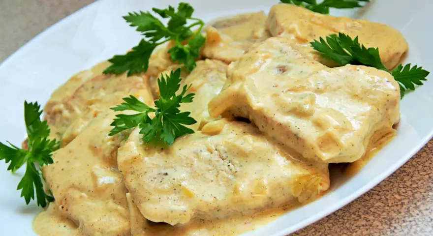 Filet z indyka w sosie śmietanowym, udekorowany natką pietruszki, prezentuje się apetycznie na białym talerzu.
