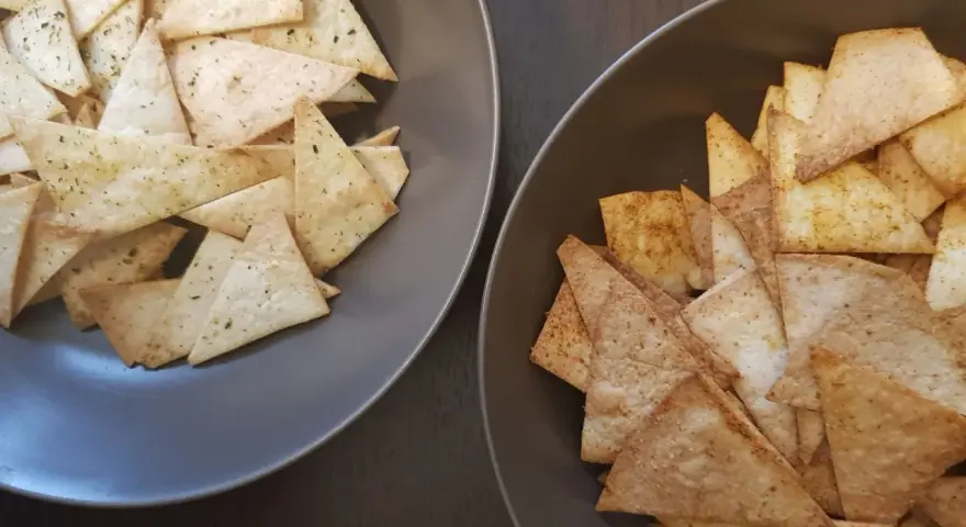 Dwa talerze pełne chrupiących chipsów z tortilli, jedne z ziołami, drugie z przyprawami. Idealne na przekąskę!