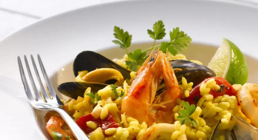 Pyszne risotto z owocami morza: krewetki, małże, kalmary i ryż, udekorowane natką pietruszki i ćwiartką limonki.