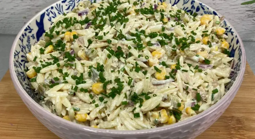 Pyszna sałatka z tuńczykiem i makaronem orzo, z kukurydzą i szczypiorkiem, w ozdobnej misce.