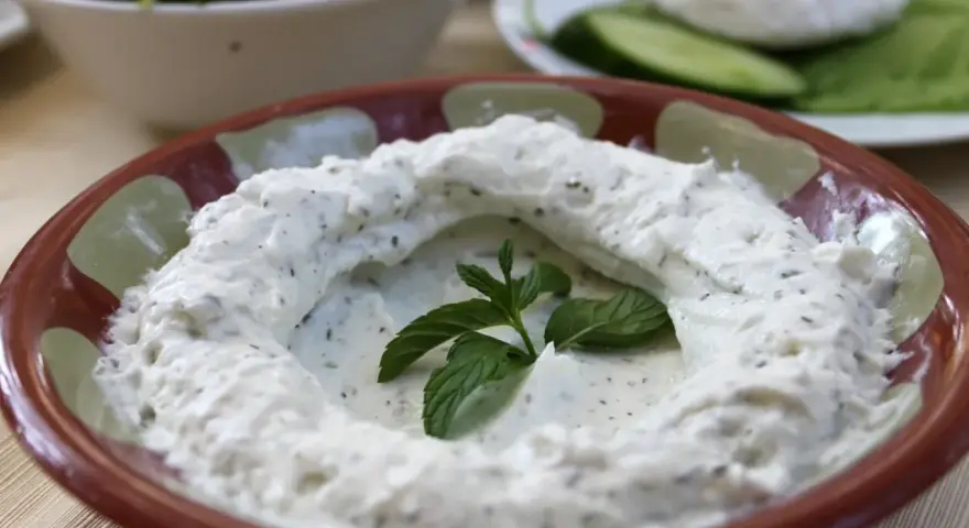 Kremowy labneh co to? Gęsty, biały serek z ziołami, udekorowany świeżą miętą, w glinianej misce.