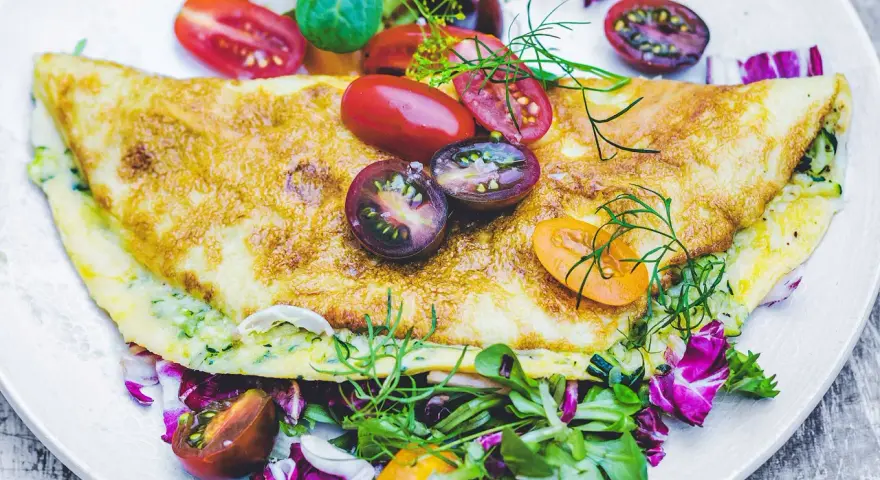 Złocisty omlet z cukinią, podany z kolorową sałatką i pomidorkami koktajlowymi. Pyszne i zdrowe śniadanie.