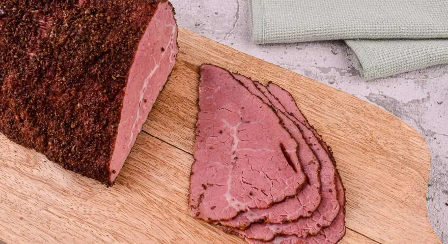 Pastrami co to? Aromatyczny, peklowany i wędzony kawałek wołowiny, pokrojony w cienkie plastry, leżący na desce.