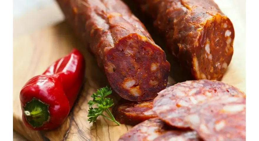Kawałki pikantnego chorizo, czerwona papryczka i natka pietruszki na desce. Dowiedz się, chorizo co to jest!