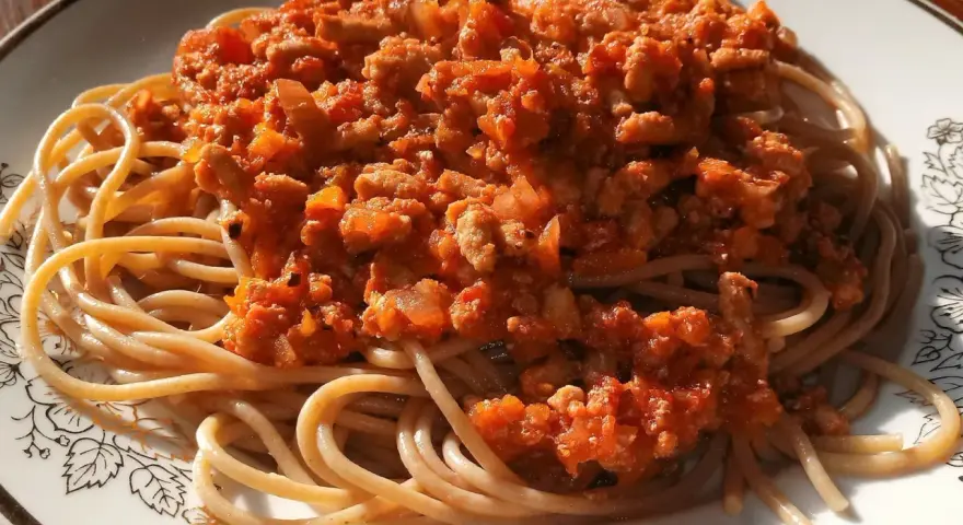 Porcja pysznego spaghetti bolognese z aromatycznym sosem mięsnym i pomidorowym, podana na talerzu z ozdobnym wzorem.