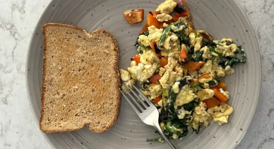 Pyszny pomysł na śniadanie: jajecznica ze szpinakiem i papryką na grzance z pełnoziarnistego chleba.