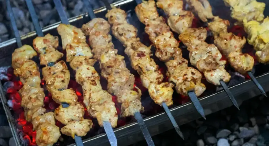 Aromatyczny kebab z kurczaka na rozżarzonych węglach. Soczyste kawałki mięsa pieką się na szpikulcach, tworząc apetyczny widok.