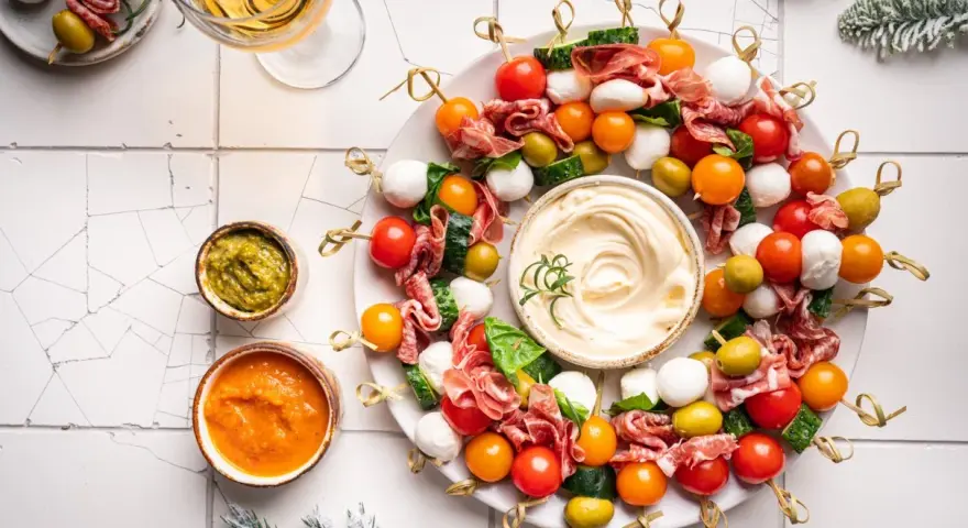 Kolorowe przystawki na zimno w kształcie wieńca, z mozzarellą, pomidorkami, oliwkami i salami, podane z dipami.