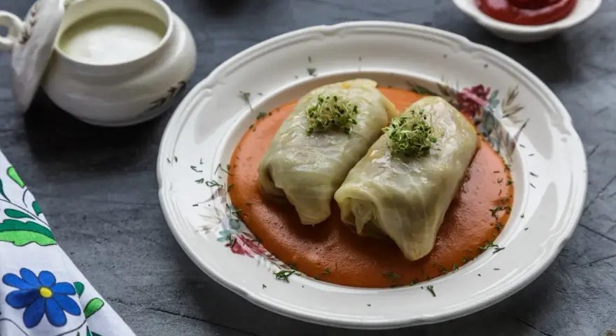 Dwa gołąbki w sosie pomidorowym, udekorowane kiełkami. Pytanie brzmi: czy gołąbki można mrozić? Obok sos śmietanowy i ketchup.