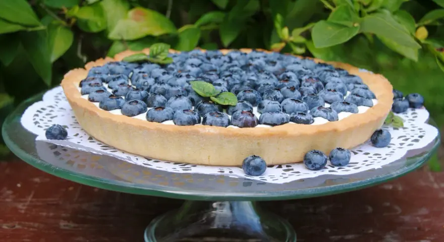 Pyszna tarta z borówkami, udekorowana listkiem mięty, prezentuje się apetycznie na szklanej paterze.