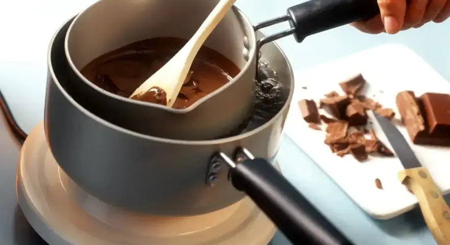 Delikatne topienie czekolady w kąpieli wodnej, by uzyskać idealną konsystencję. Drewniana łyżka miesza płynną masę.