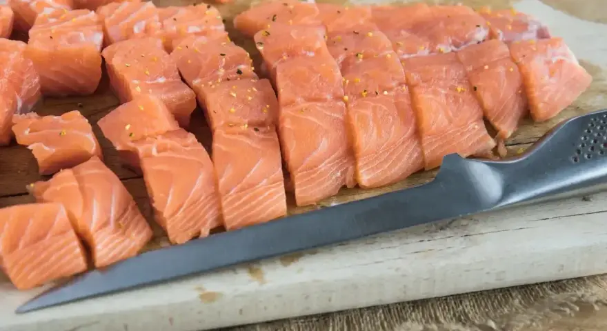 Pokrojony łosoś, idealny jaki łosoś do sushi, leży na desce obok noża.