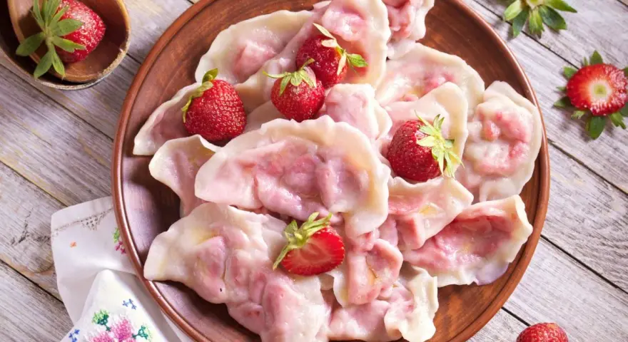 Pyszne pierogi z truskawkami, ozdobione świeżymi owocami, wyglądają apetycznie na glinianym talerzu.