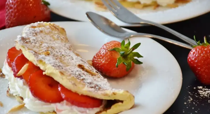 Słodki omlet z bitą śmietaną i truskawkami, posypany cukrem pudrem. Idealny przepis na deser.