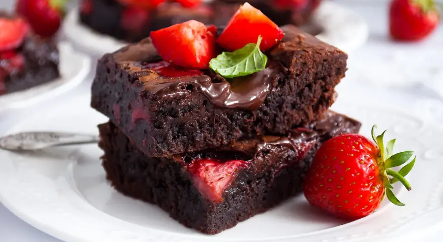 Pyszne brownie z truskawkami, polane czekoladą i ozdobione listkiem mięty. Idealne na deser.