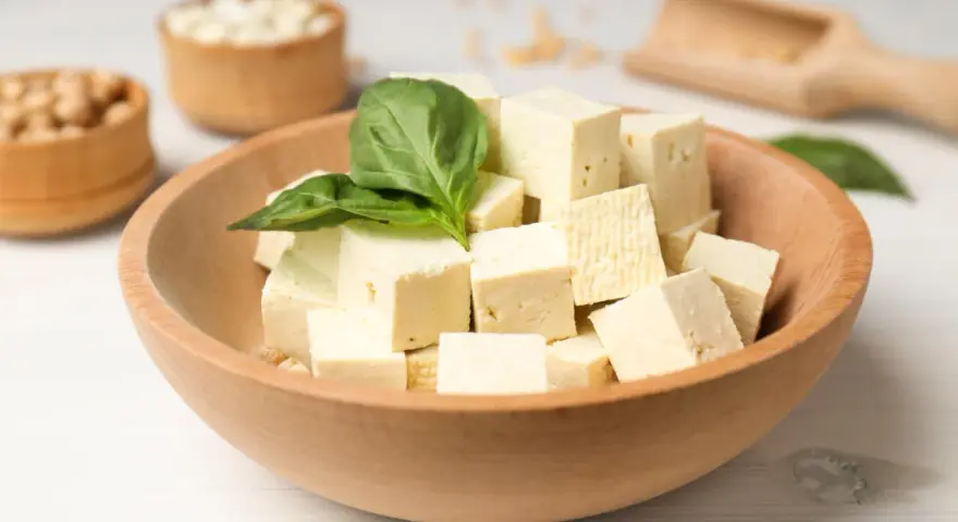 Kostki tofu w drewnianej misce z bazylią. Czy tofu można jeść na surowo? Tak, to idealny składnik do sałatek i przekąsek.