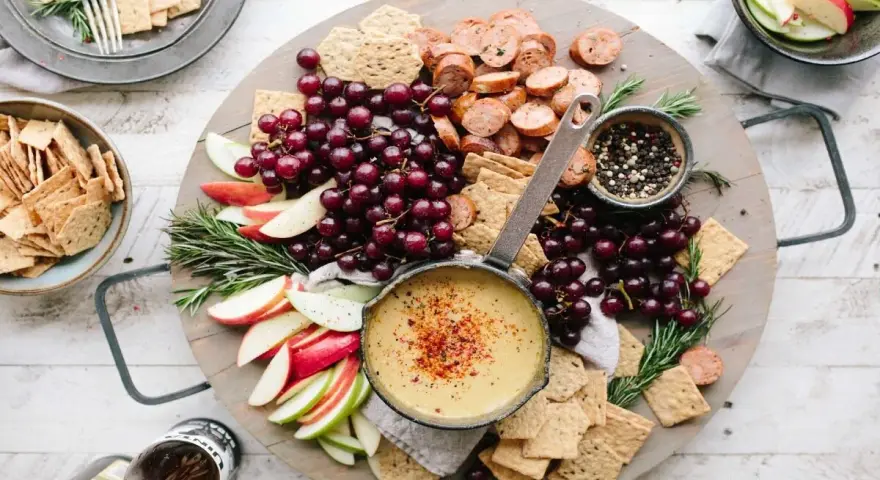 Idealne menu na sylwestra w domu: deska z serkiem, winogronami, jabłkami, kiełbaską i krakersami.