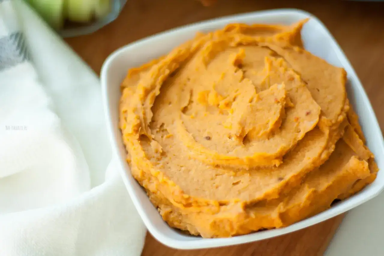 Pomarańczowy hummus z suszonymi pomidorami, podany w białej miseczce, z widocznymi kawałkami pomidorów.