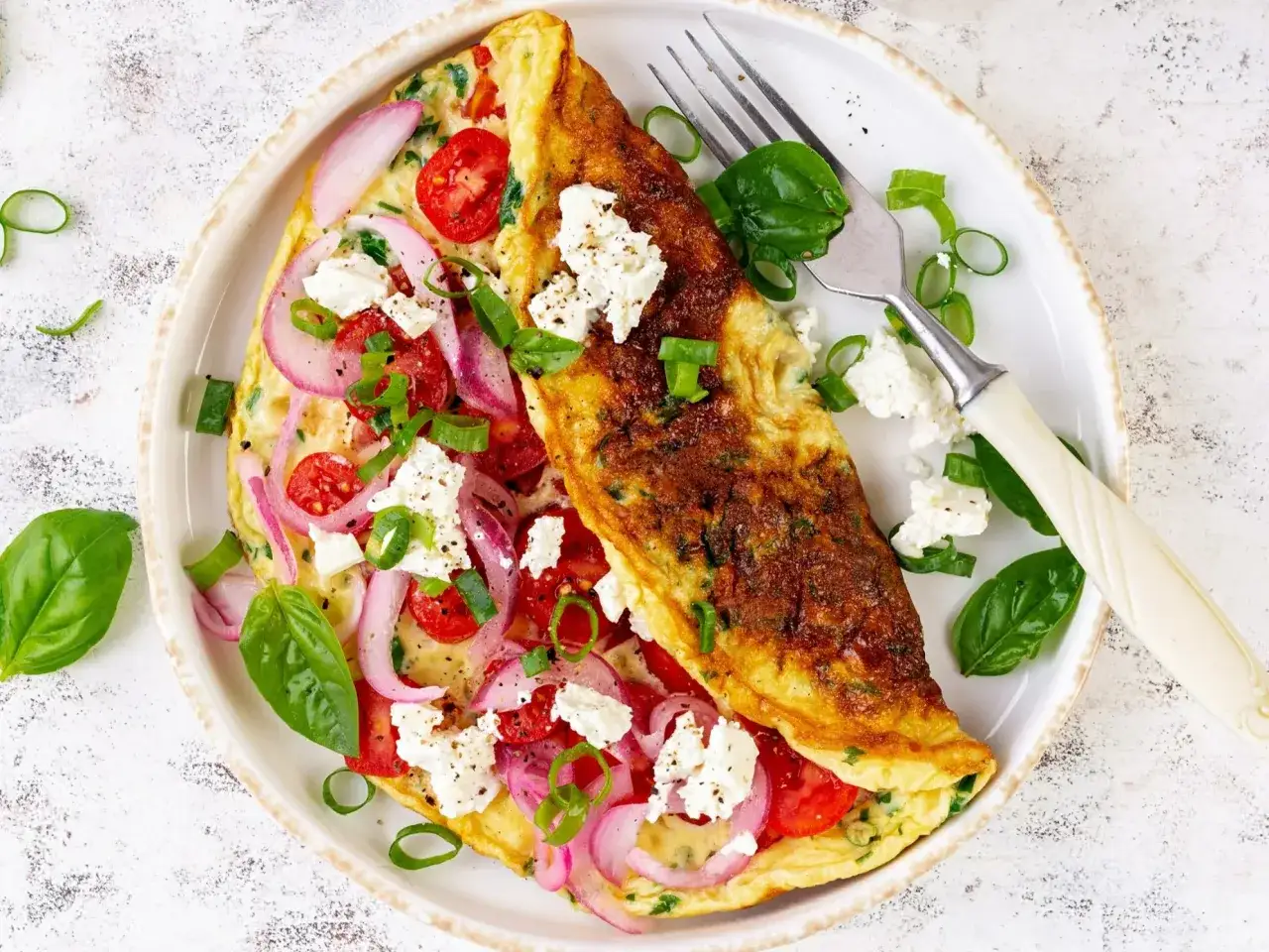 Pyszny omlet z warzywami: pomidorki, czerwona cebula, ser feta i szczypiorek. Idealny na śniadanie.