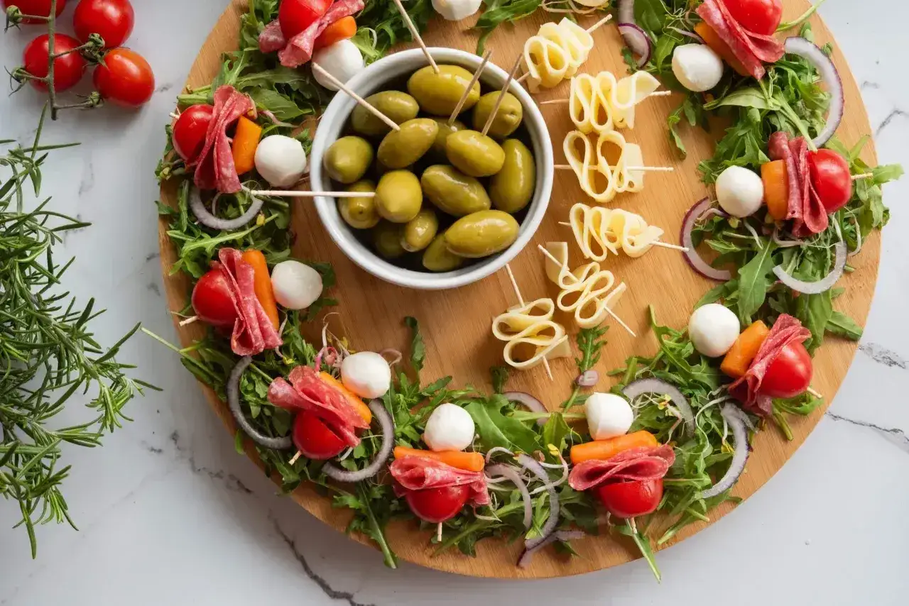 Kolorowe sałatki na imprezę: szaszłyki z pomidorkami, mozzarellą, salami i marchewką, oliwki i ser na drewnianej desce.