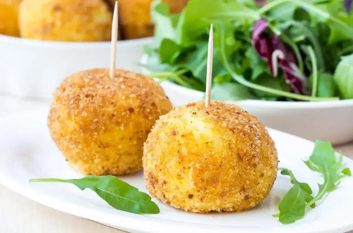 Arancini co to? Złociste, chrupiące kulki ryżowe z wykałaczkami, podane z sałatką. Pyszna przekąska.