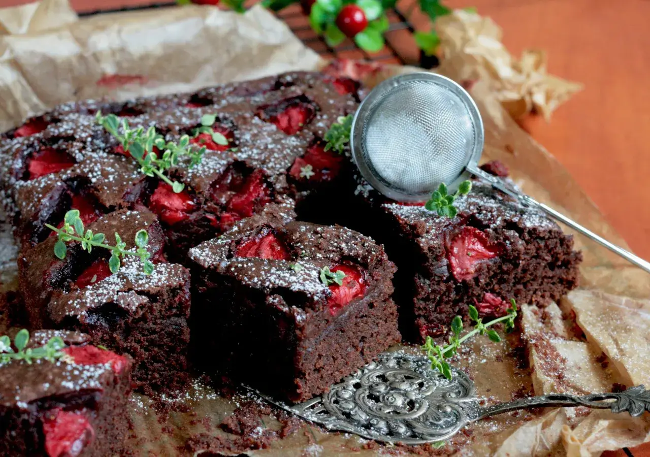 Pyszne brownie z truskawkami, posypane cukrem pudrem i udekorowane gałązkami tymianku. Idealne na deser!