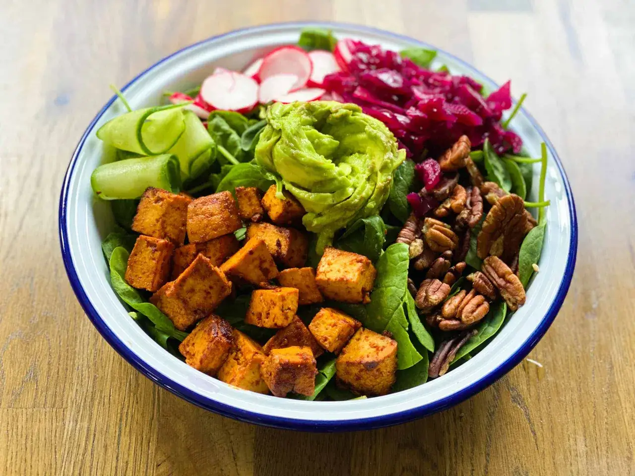 Kolorowa sałatka z pieczonymi kostkami tofu, awokado, rzodkiewką, ogórkiem i orzechami. Czy tofu można jeść na surowo? W tej wersji jest pieczone, ale można też próbować na zimno.