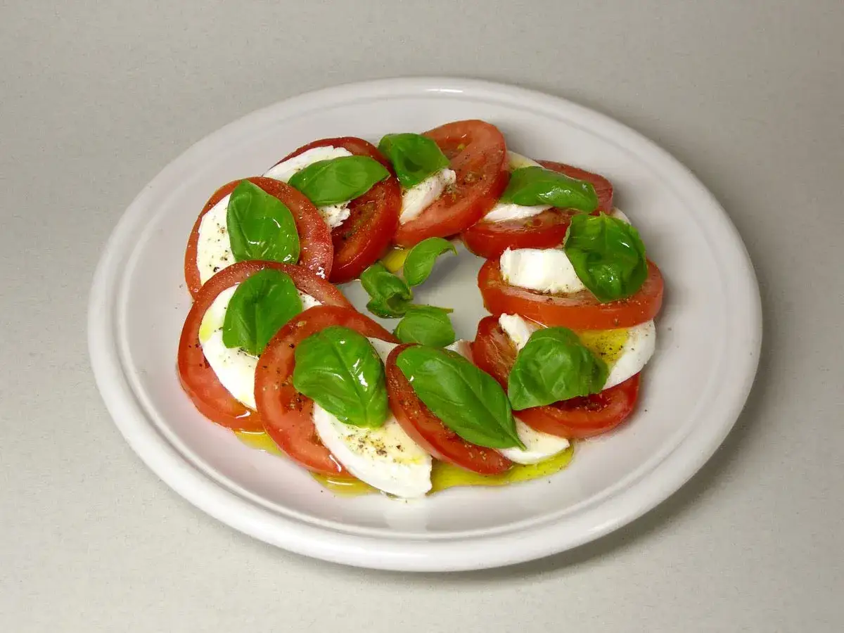 Kółko z plastrów pomidorów i mozzarelli, ozdobione listkami bazylii. Pyszne pomidory z mozzarellą na talerzu.