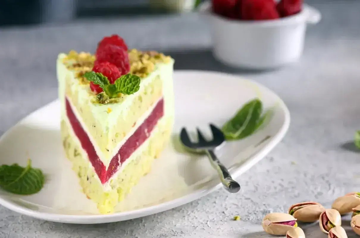 Pyszny tort pistacjowo malinowy z malinami i miętą na talerzu.
