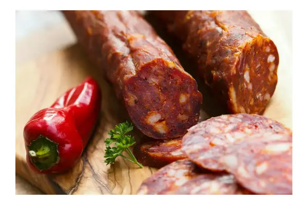 Kawałki pikantnego chorizo, czerwona papryczka i natka pietruszki na desce. Dowiedz się, chorizo co to jest!