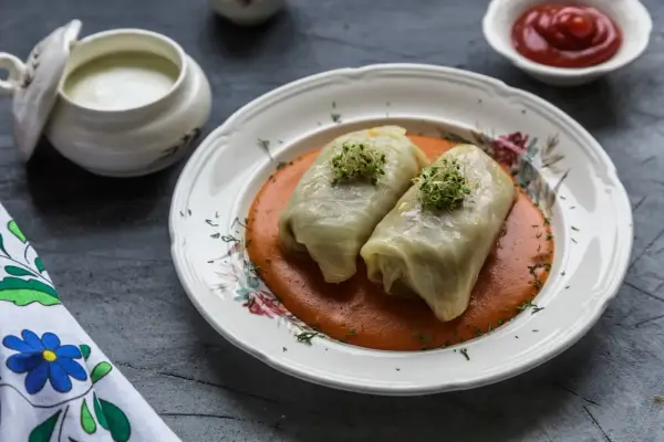 Dwa gołąbki w sosie pomidorowym, udekorowane kiełkami. Pytanie brzmi: czy gołąbki można mrozić? Obok sos śmietanowy i ketchup.